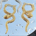 Gold snake-shaped earrings on a textured blue surface.