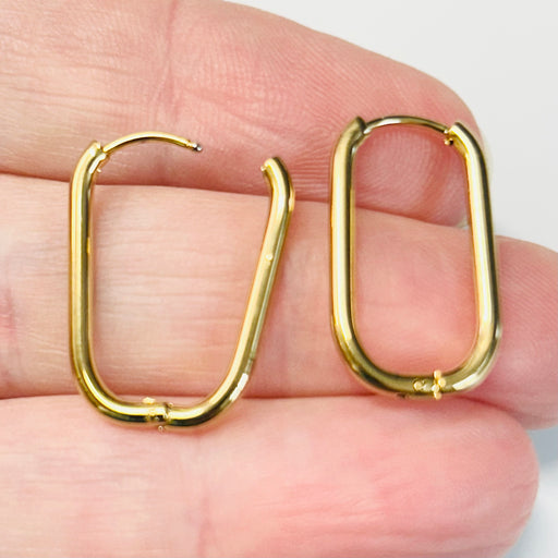 Gold hoop earrings held between fingers against a neutral background