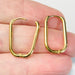 Gold hoop earrings held between fingers against a neutral background