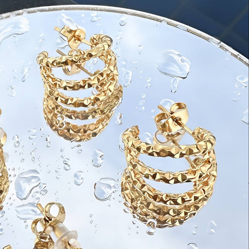 Gold hoop earrings on a textured surface with water droplets