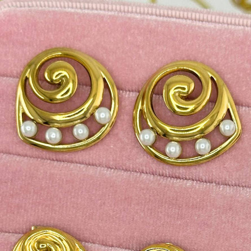 Set of gold earrings with pearls and gemstones on a pink velvet surface