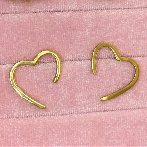 Gold heart-shaped earrings on a pink textured background