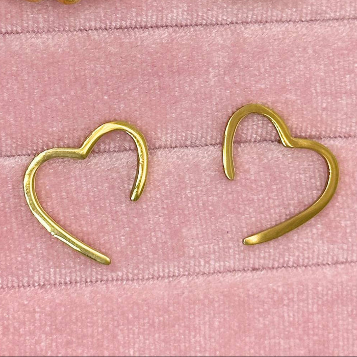 Gold heart-shaped earrings on a pink textured background