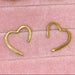 Gold heart-shaped earrings on a pink textured background