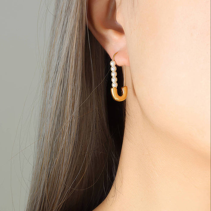 Close-up of an ear wearing a gold earring with pearls against a neutral background