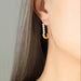 Close-up of an ear wearing a gold earring with pearls against a neutral background