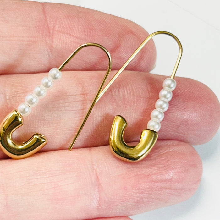 Gold earrings with pearl beads held between fingers on a light background