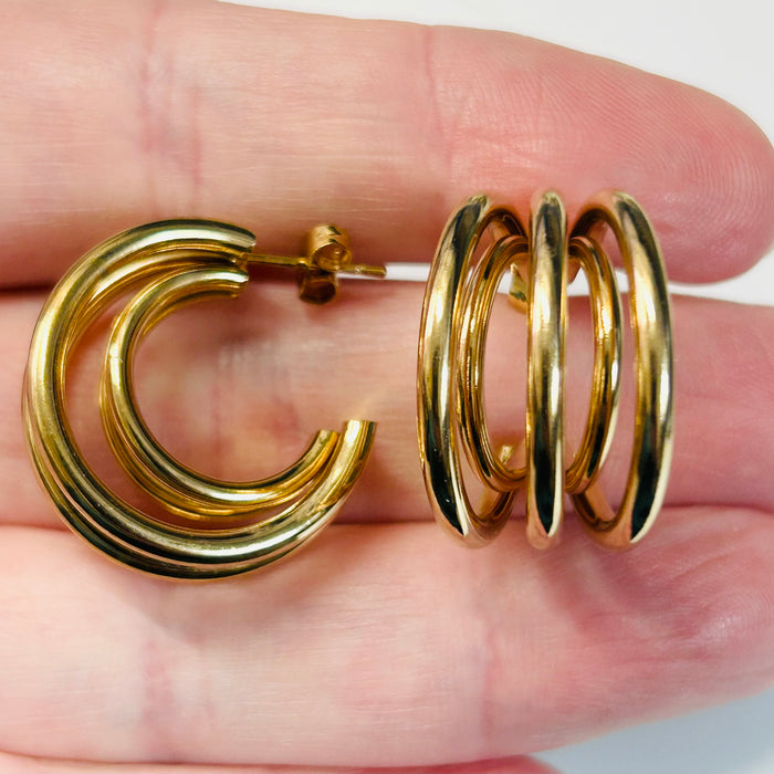 Gold hoop earrings held between fingers against a neutral background