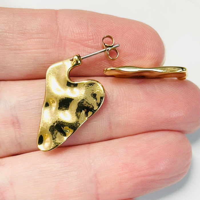 Gold heart-shaped earring on a hand with a white background