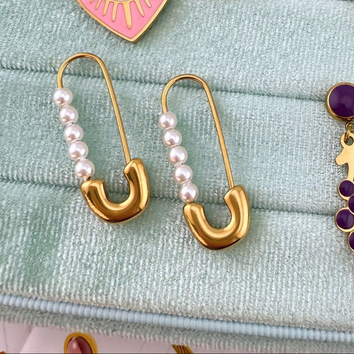 Gold safety pin earrings with pearl beads on a textured fabric background