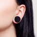 Close-up of an ear wearing black round earrings with a neutral background
