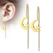 Gold earrings with moon and star designs hanging from an ear on a white background